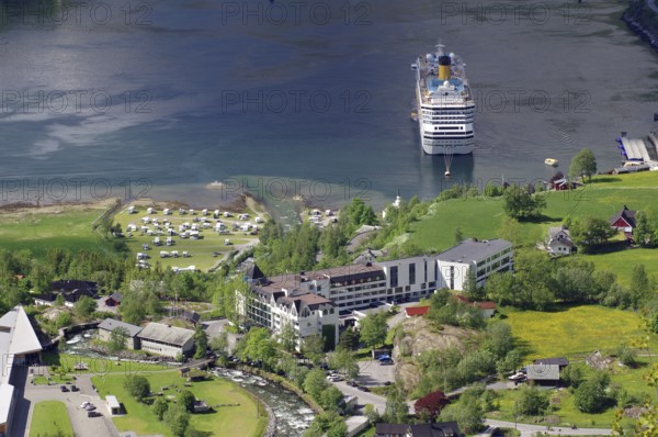 A large cruise ship is moored on a shore with many buildings and green meadows and trees, Geiranger and Geirangerfjord, Fjordland, Norway, Europe