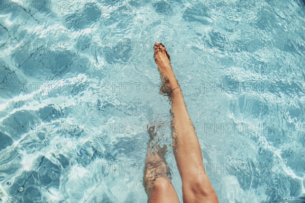 Beautiful legs of a woman splashing in a turquoise-coloured pool