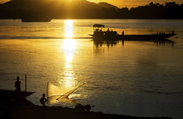 Fishermen fishing next to boats in the Brahmaputra river, during sunset in Guwahati, Assam, India on 1 August 2023