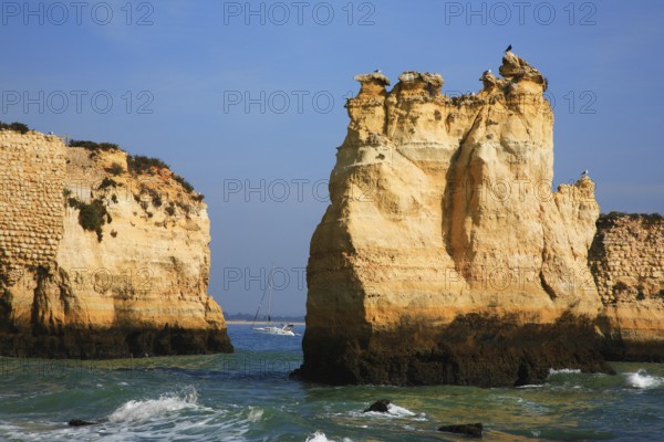 Praia do Pinhao, Lagos, Algarve, Portugal, Majestic coastal landscape with steep cliffs and a narrow passage to the calm sea, where a boat sails in the distance, Europe