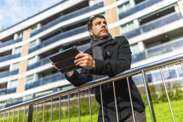 Low angle view portrait of a casual adult caucasian businessman using digital tablet leaning on rail at street