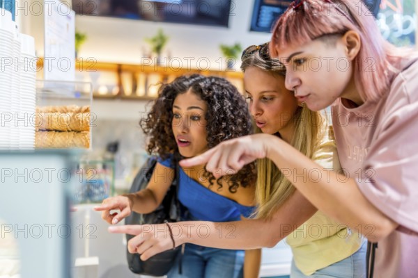 Side view of three diverse modern women pointing at ice cream glass counter choosing a flavor