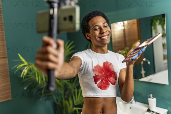 Happy latin gay man using mobile phone while recording makeup tutorial