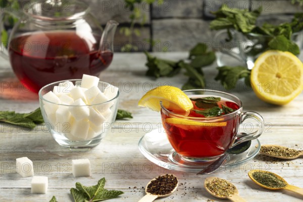 Teapot and glass with tea, lemon and mint, next to sugar and teas on a table