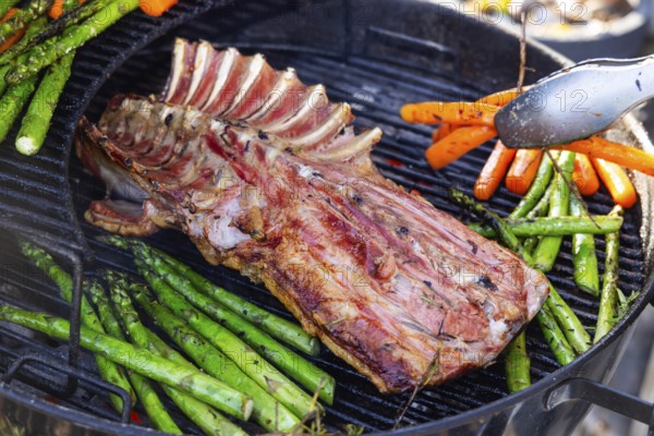 Barbecue with Easter roast. Rack of lamb and green asparagus grilled on an outdoor kettle barbecue. Meat and vegetarian vegetables. Baden-Württemberg, Germany, Europe