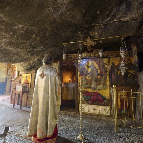 A clergyman stands in front of a scenic decorated room in a church during a service, rock grotto, Monastery of Apokalipsis, Patmos, Dodecanese, Greek Islands, Greece, Europe