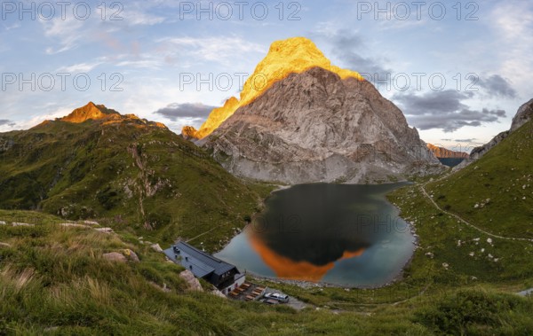 Alpenglow at Seekopf or Monte Capolago, reflection in Lake Wolayersee with Alpine Club hut Wolayerseehütte, mountain landscape with green meadows and mountain lake at sunset, Carnic Alps, Carnic High Trail, Carinthia, Austria, Europe