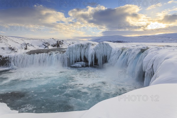 Icy waterfall and rapids in front of a mountain landscape, cloudy mood, snow, Godafoss, Isla
