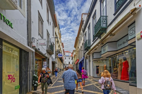 People walk through a busy shopping street with modern shops and historic buildings under a bright sky, Ponta Delgada, Sao Miguel Island, Azores, Portugal, Europe