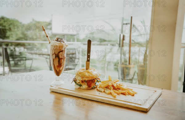 Close up of burger with fries and milkshake on wooden board with space for text. Delicious big burger with french fries and milkshake on restaurant table