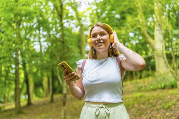 Young caucasian female tourist using phone and listening to music while hiking in the forest