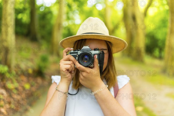 Frontal portrait of a caucacsian young woman traveler taking photos in the forest hiding with the camera