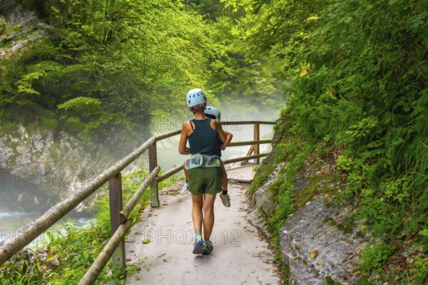 Mother carrying her child while hiking on a misty summer day in vintgar gorge near bled, slovenia, enjoying a scenic walk through nature