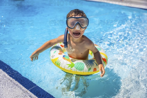 Happy playful caucasian boy with snorkel goggles and rubber ring on the swimming pool