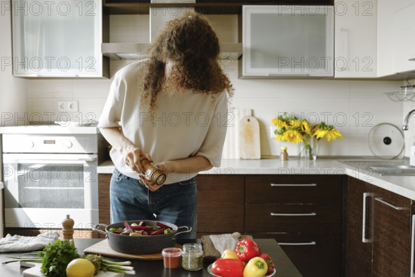 Woman sprinkles salt from manual spice mill on vegetables in a baking pan