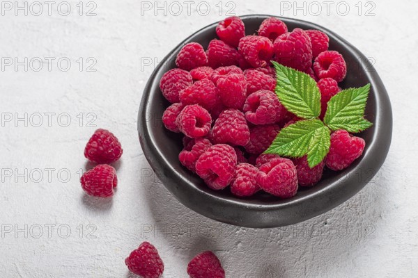 Fresh raspberries, on a black plate, with leaves, top view, on a white table