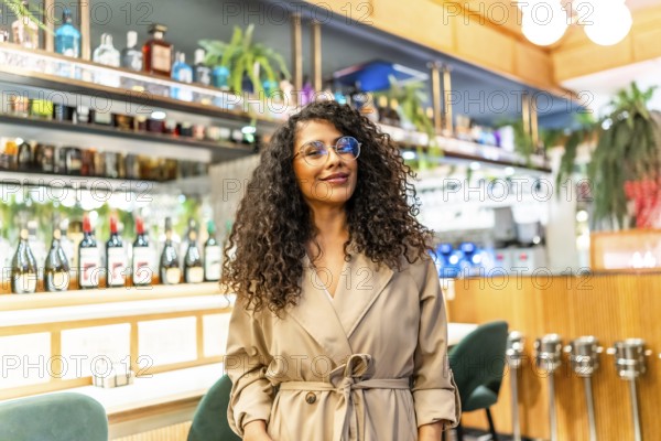 Beauty chic latin woman with curly hair and eyeglasses standing in a cafeteria smiling at camera