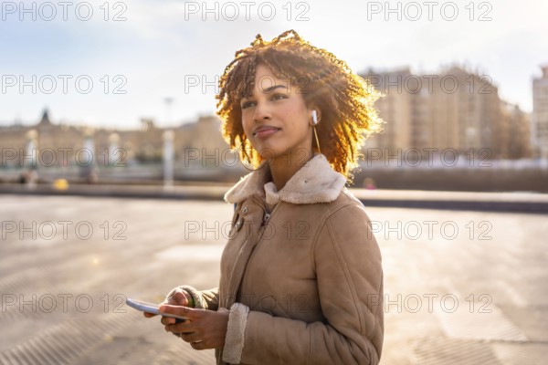 Latin beauty woman listening to music with earbuds and mobile phone outdoors in the city during sunset