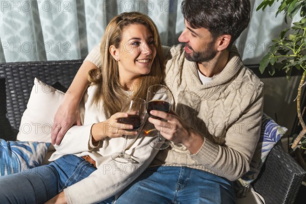 Romantic couple toasting with red wine, enjoying a cozy moment together on a comfortable sofa