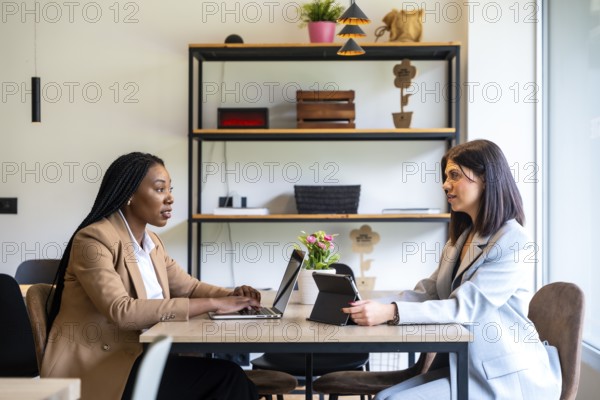 Two businesswomen are having a business meeting in a hotel lobby, working on their laptops and digital tablets