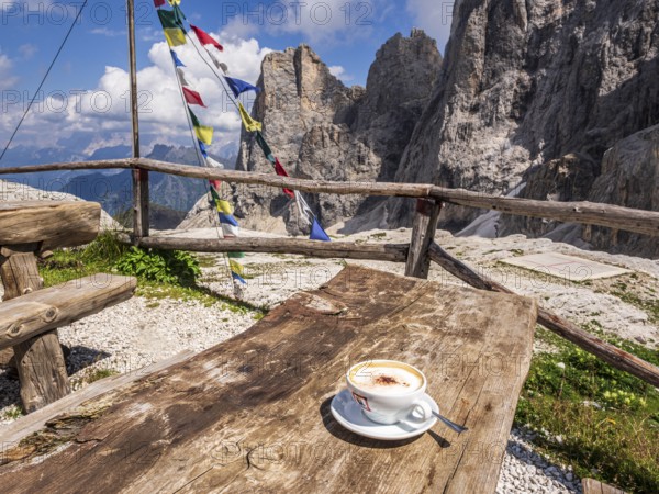 A cup of cappuccino, tibetian flag of prayer, mountain hut Rifugio Mulaz, Pala mountain group in the back, dolomites, Trentino, Italy, Europe