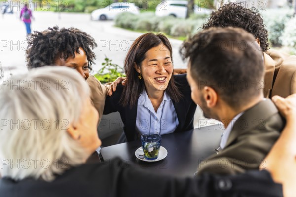 Successful team of multi-ethnic business people celebrating embracing form the shoulder sitting in a cafeteria