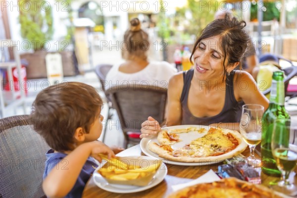 Mother and son sharing a meal of pizza and french fries at an outdoor restaurant, enjoying their summer vacation together