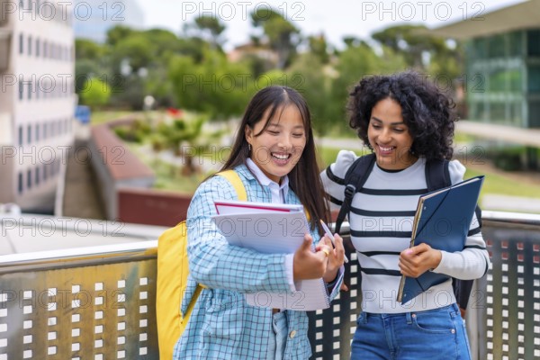 Two beauty young smiling multi-ethnic students reading notes standing outside the university campus