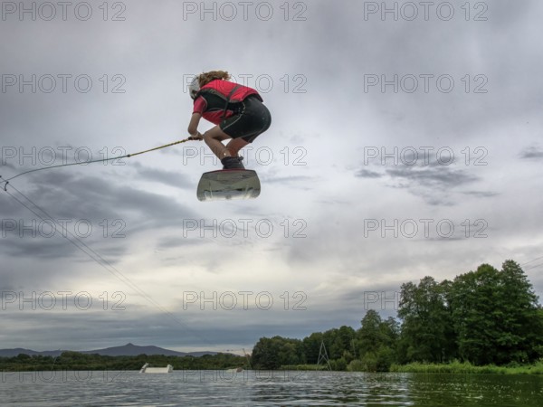 Boy or girl flies over the lake, jump with wakeboard, red life jacket, water skiing in wakepark, Stráž pod Ralskem, Czech Republic, Europe