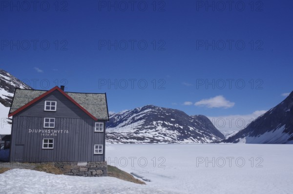 Mountain hut in a snow-covered late winter landscape, surrounded by mountains and a frozen lake, under a clear blue sky, Langevatn, Geiranger, Fjell, Norway, Europe