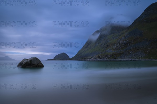 Landscape on the beach at Haukland. The mountains Veggen and Mannen on the right. The sky is cloudy. The sea is blurred due to the long exposure. Early summer, at night. Haukland Beach, Haukland, Vestvagoya, Lofoten, Norway, Europe