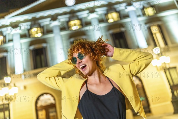 Cool happy caucasian woman in yellow jacket and sunglasses dancing in the city at night