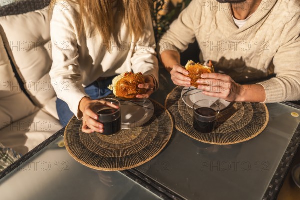Couple sharing a relaxed moment, eating burgers and drinking beverages at a glass table, creating a cozy and intimate atmosphere