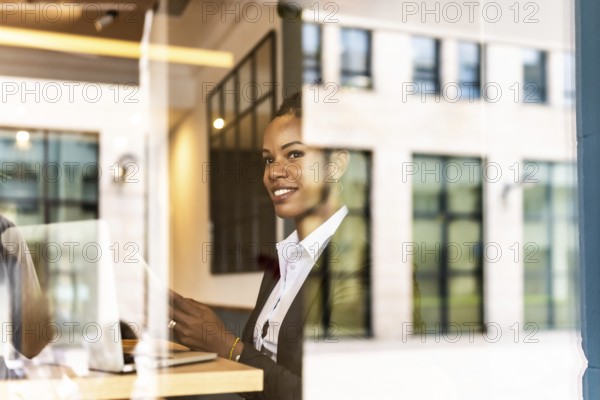 Views from outside the window of a distracted businesswoman using mobile phone working in a modern cafeteria in the financial district
