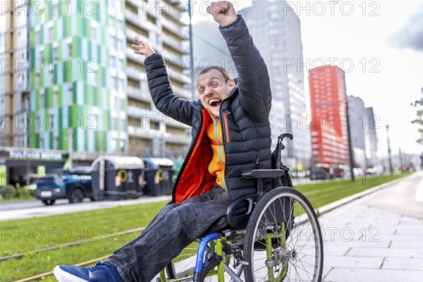Young man in a wheelchair, raising his arms in celebration, embracing freedom and joy in a vibrant urban setting filled with modern architecture