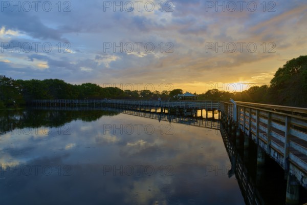 Peaceful lake reflecting the sky at sunset with a wooden bridge stretching across, surrounded by trees and a tranquil atmosphere, Wakodahatchee Wetlands, Delray Beach, Florida, USA, North America