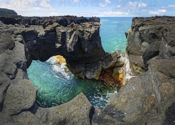 Panoramic view of rugged lava rock formations with a natural arch over turquoise sea under blue sky, A Porta do Diabo, Sao Miguel Island, Azores, Portugal, Europe