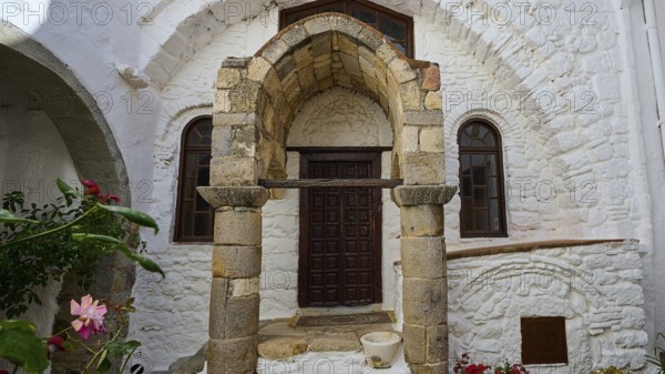 Entrance of a building with ancient columns and a round arch, surrounded by flowers and stone walls, Inside the monastery, Agiou Theologou Monastery, Chora, Patmos, Dodecanese, Greek Islands, Greece, Europe