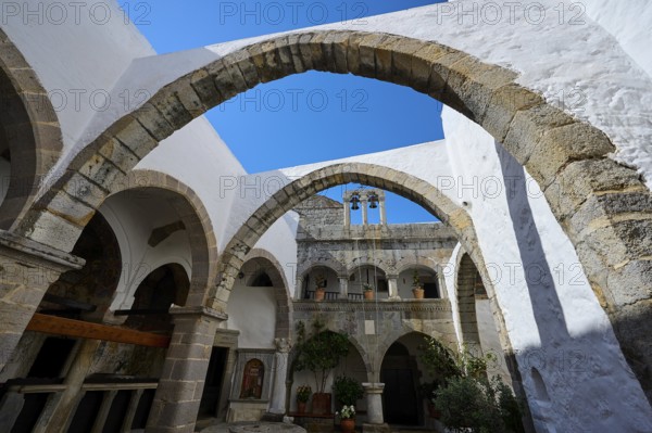 Inner courtyard of a monastery with stone arches and Mediterranean architecture under a blue sky, Inside the monastery, Agiou Theologou Monastery, Chora, Patmos, Dodecanese, Greek Islands, Greece, Europe