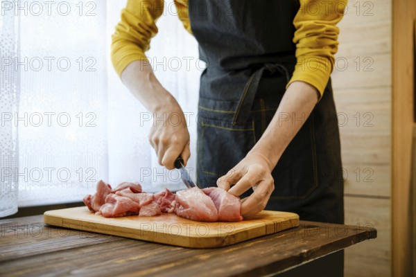 Unrecognizable man cuts pork meat into large pieces in the kitchen