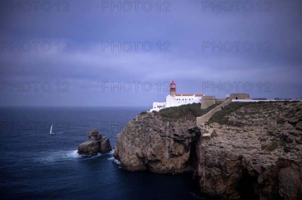 Sailing boat in front of the lighthouse Farol do Cabo de São Vicente, Cape St. Vincent, Sagres, steep coast, Atlantic Ocean, Algarve, Portugal, Europe