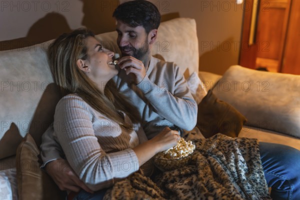 Couple enjoying a cozy night in, sharing popcorn and watching a movie together on the sofa