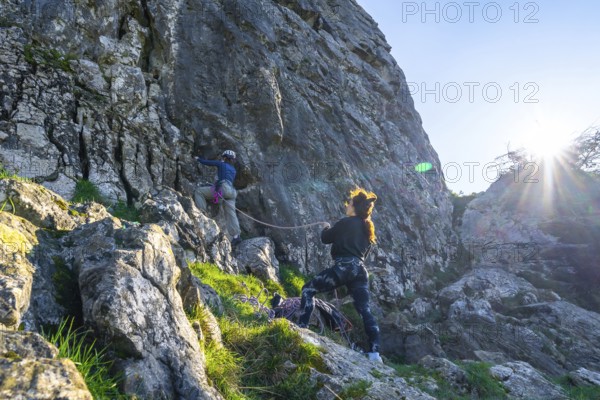 Two female rock climbers scaling a steep cliff face, illuminated by bright sunlight, showcasing teamwork and determination in outdoor adventure