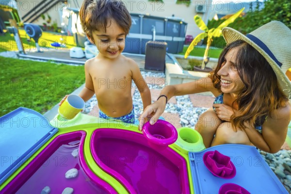 Mother and son enjoying quality time together, playing with a colorful water table in their backyard during summer vacation