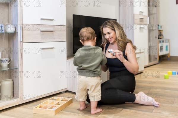 Smiling mother showing toy car to her baby boy while playing together on the floor in the living room
