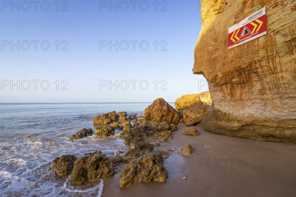 ROCKFALL UNSTABLE CLIFFS, KEEP A SAFE DISTANCE is written in English on a warning sign in Portugal on the cliffs of the Atlantic Ocean. Rocks and stones break out here again and again and injure people., Albufeira, Faro, Portugal, Europe