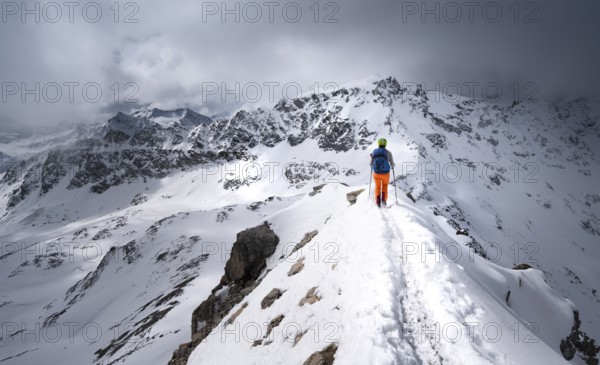 Mountaineer descending the narrow ridge of Piz Laviner, view of mountain panorama in wintry mountain landscape with dramatic clouds, Grisons Haute Route, Albula Alps, Rhaetian Alps, Grisons, Eastern Switzerland, Switzerland, Europe