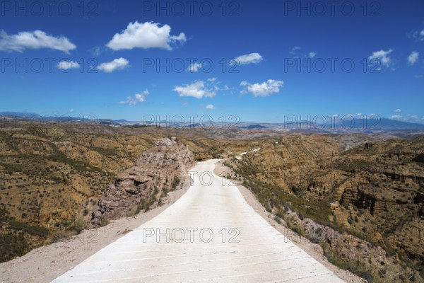 A long straight road leads through a vast desert landscape with mountains and a clear blue sky, Gorafe desert, Granada, Andalusia, Spain, Europe