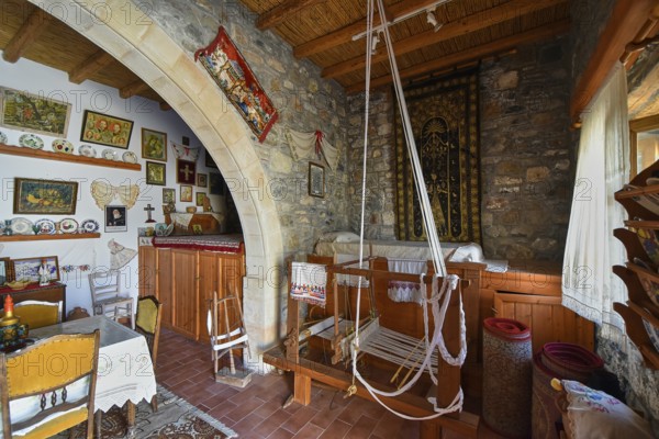 A traditionally furnished interior with stone walls, a wooden ceiling and a loom in the centre, surrounded by handicrafts and decorations, Folklore Museum, Asklipio village, Asklipion, Rhodes, Dodecanese, Greek Islands, Greece, Europe