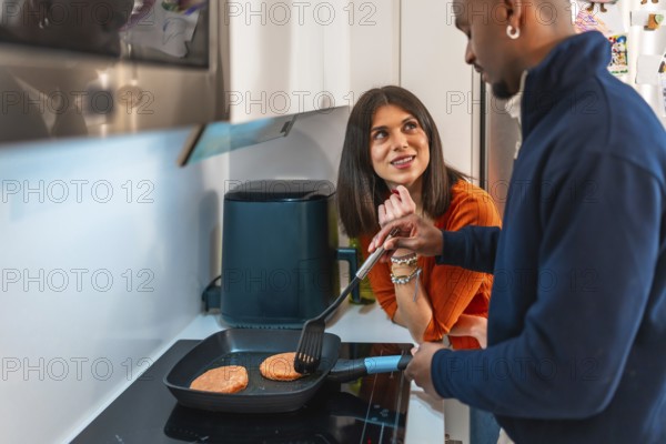 Happy multiethnic couple preparing burgers in a pan in their modern kitchen, enjoying their time together